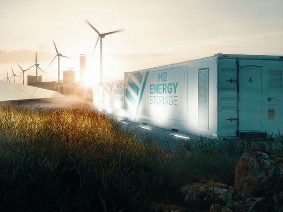 A hydrogen energy storage container marked 'H2 ENERGY STORAGE' in turquoise color, set against a sunset background with wind turbines and industrial buildings. Ground lighting illuminates the container while tall grass grows in the foreground.