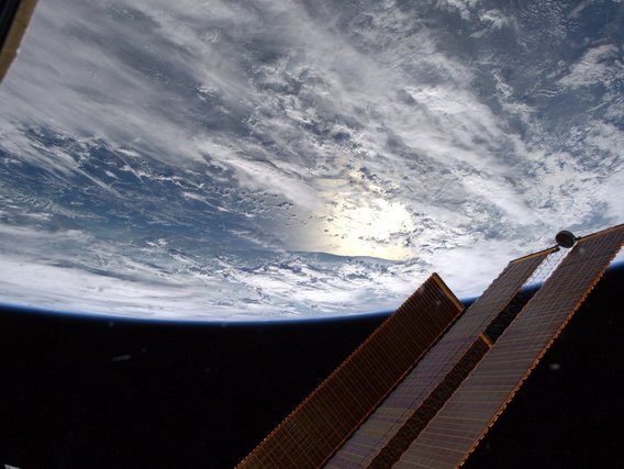 lick von der ISS auf die gekrümmte Erde mit Wolken und Solarpaneelen im Vordergrund.