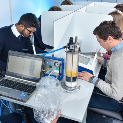 Mehrere Studierende arbeiten an einem Laborexperiment mit einer Wasserfiltrationsanlage. Ein Laptop überwacht den Prozess, während die Teilnehmer an Einzelarbeitsplätzen mit Trennwänden sitzen.