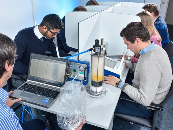 Mehrere Studierende arbeiten an einem Laborexperiment mit einer Wasserfiltrationsanlage. Ein Laptop überwacht den Prozess, während die Teilnehmer an Einzelarbeitsplätzen mit Trennwänden sitzen.