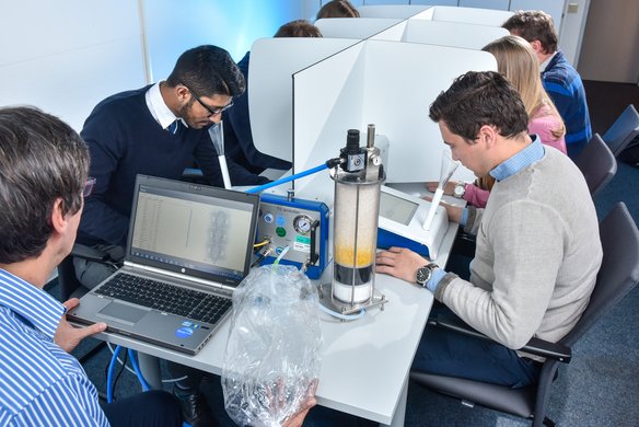Mehrere Studierende arbeiten an einem Laborexperiment mit einer Wasserfiltrationsanlage. Ein Laptop überwacht den Prozess, während die Teilnehmer an Einzelarbeitsplätzen mit Trennwänden sitzen.