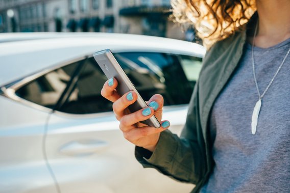 Frau mit Smartphone vor einem Auto