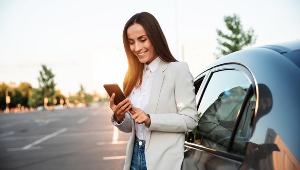 Frau steht neben einem Auto und benutzt ein Smartphone