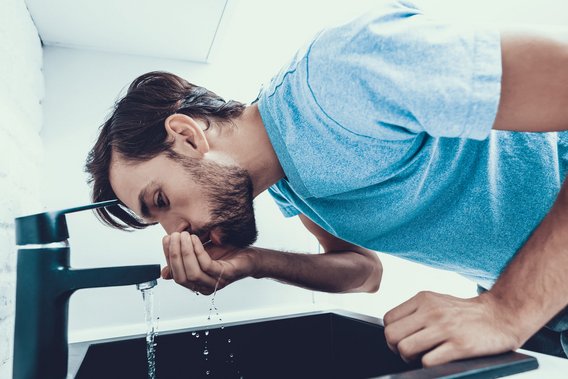 Person beugt sich über ein Waschbecken und schöpft Wasser aus einem Wasserhahn.