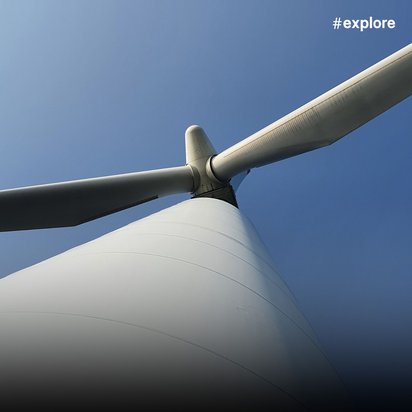 Blick von unten auf eine weiße Windkraftanlage mit drei Rotorblättern gegen strahlend blauen Himmel. Die Perspektive betont die imposante Größe der nachhaltigen Energieanlage und ihre moderne, schlanke Konstruktion.