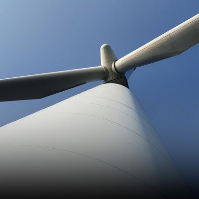 Blick von unten auf eine weiße Windkraftanlage mit drei Rotorblättern gegen strahlend blauen Himmel. Die Perspektive betont die imposante Größe der nachhaltigen Energieanlage und ihre moderne, schlanke Konstruktion.