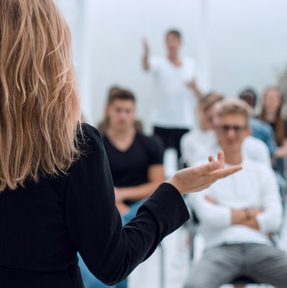 Person steht im Vordergrund und leitet ein Seminar