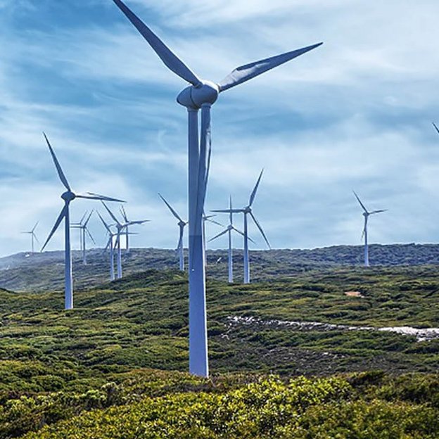 Das Bild zeigt mehrere Windenergieanlagen, die Nahe einer Küste auf einer hügeligen Landschaft stehen