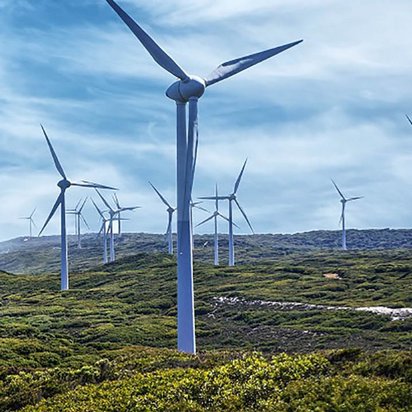 Windenergie Header Das Bild zeigt mehrere Windenergieanlagen, die Nahe einer Küste auf einer hügeligen Landschaft stehen