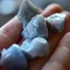 Eine Hand hält rohe, natürliche, klumpige blaue Calcit-Mineralien.