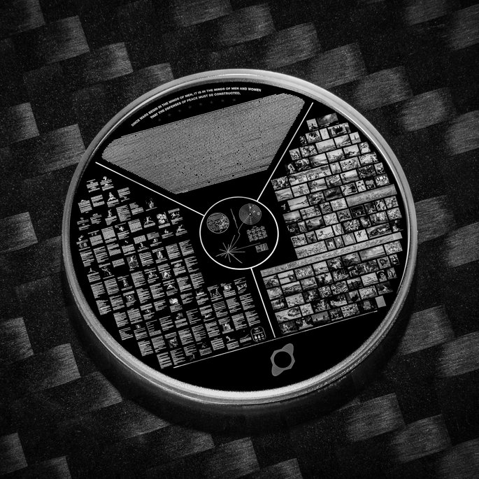 Eine runde Platte mit einer Vielzahl von Informationen und Bildern, die eine kulturelle Botschaft darstellen. Die Platte ist in mehrere Abschnitte unterteilt, darunter Text, Diagramme und Fotos, die verschiedene Aspekte der Menschheit und Wissenschaft zeigen. Sie liegt auf einer strukturierten Oberfläche.