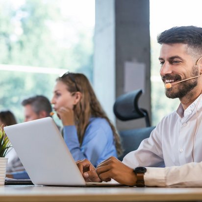 Callcenter-Mitarbeiter im Büro beantwortet Anrufe und arbeitet am Laptop