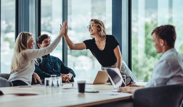 Zwei Kolleginnen geben sich ein High-Five während eines Meetings in einem modernen Konferenzraum.