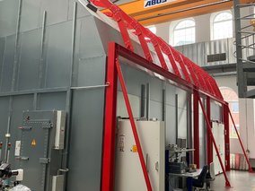 Ein großer roter Metallrahmen mit einer Abus-Kranbrücke in einer industriellen Fertigungshalle mit grauen Wänden.