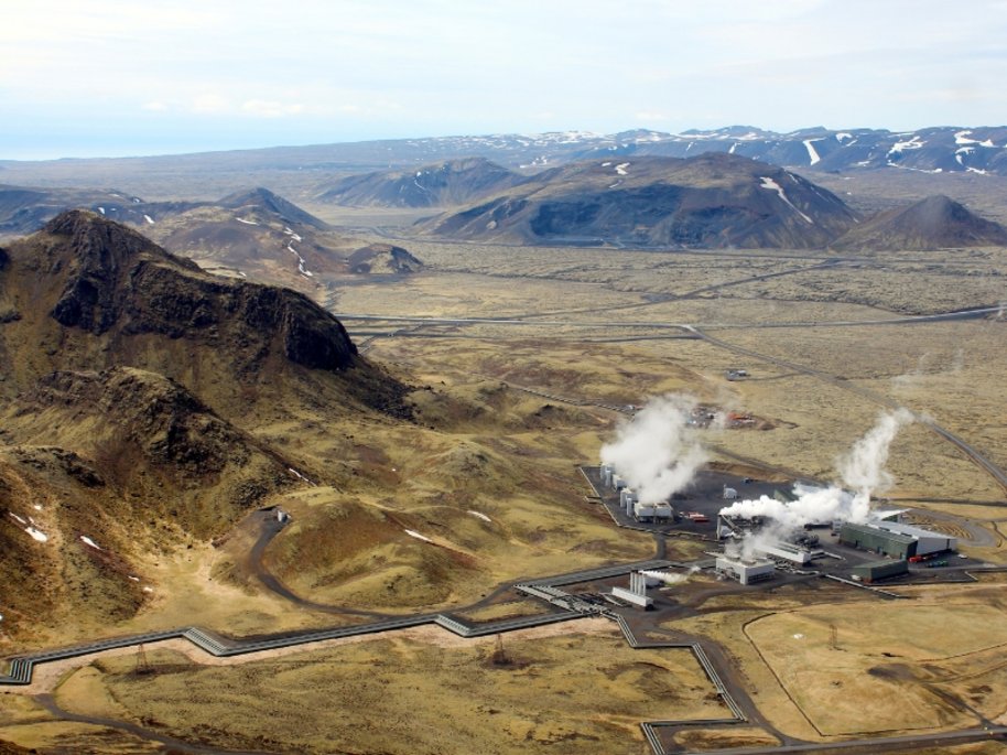 Geothermisches Kraftwerk in Island, eingebettet in eine weite, bergige Vulkanlandschaft mit Schnee und Dampf.