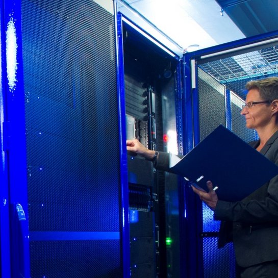 Frau steht mit einem Laptop vor Servern