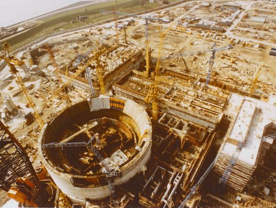 Luftaufnahme einer Kernkraftwerk-Baustelle mit charakteristischem rundem Reaktorgebäude und mehreren Baukränen.