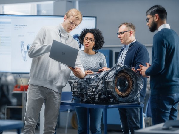 Gruppe von Ingenieuren diskutiert über ein Automobilteil in einem technischen Labor.