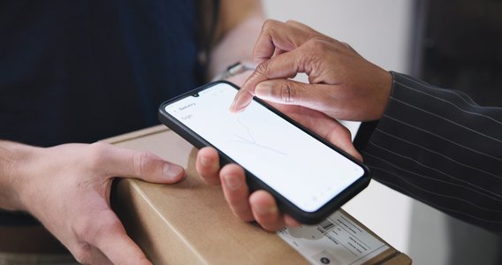 Person hält Tablet mit schwebenden E-Mail-Symbolen, Laptop und Kaffeebecher im Hintergrund.