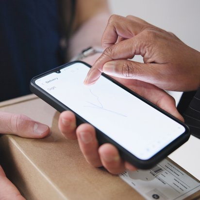 Person hält Tablet mit schwebenden E-Mail-Symbolen, Laptop und Kaffeebecher im Hintergrund.