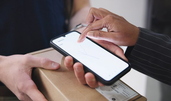 Person hält Tablet mit schwebenden E-Mail-Symbolen, Laptop und Kaffeebecher im Hintergrund.