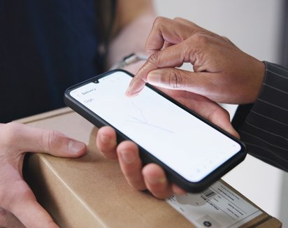 Person hält Tablet mit schwebenden E-Mail-Symbolen, Laptop und Kaffeebecher im Hintergrund.