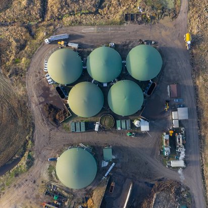 Luftaufnahme einer Biogasanlage mit mehreren runden Fermentern, umgeben von Betriebsgebäuden und Zufahrtswegen.
