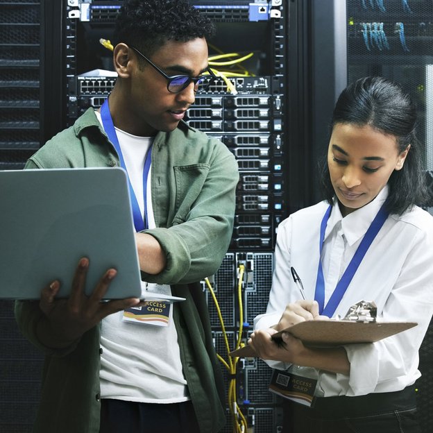 Zwei IT-Fachkräfte prüfen mit Laptop und Klemmbrett Server in einem Rechenzentrum.