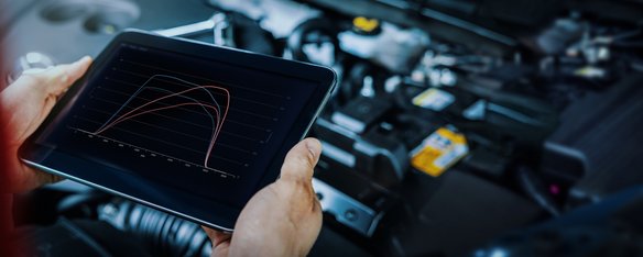 Person steht mit einem Tablet in der Hand vor einer geöffneten Haube