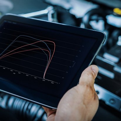 Person steht mit einem Tablet in der Hand vor einer geöffneten Haube