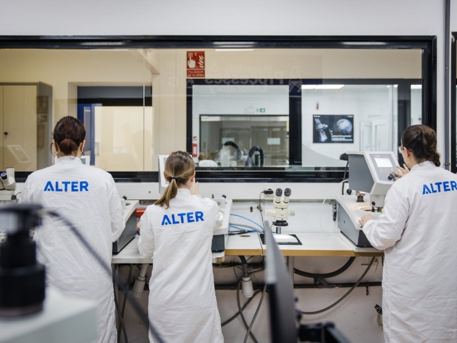 Drei Wissenschaftler in weißen ALTER-Laborkitteln arbeiten an modernen Geräten in einem sterilen Forschungslabor.
