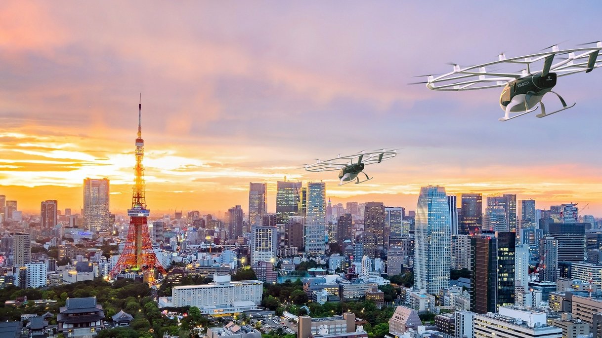Futuristische Stadtansicht von Tokio bei Sonnenuntergang mit zwei Flugtaxis über der Skyline und dem Tokyo Tower im Hintergrund.