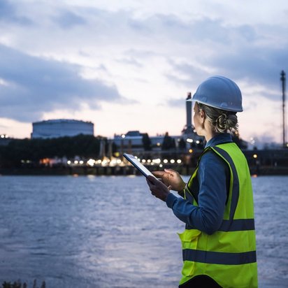 An officer in safety clothing stands by a body of water with a tablet in her hands.
