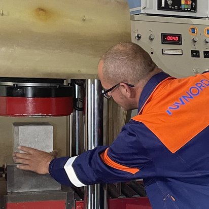 Techniker prüft Baustoffprobe in hydraulischer Presse zur Druckfestigkeitsprüfung in der Bautechnik