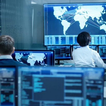 IT-Spezialisten überwachen globale Netzwerksysteme in einem Kontrollzentrum mit mehreren Bildschirmen.