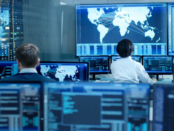 IT-Spezialisten überwachen globale Netzwerksysteme in einem Kontrollzentrum mit mehreren Bildschirmen.