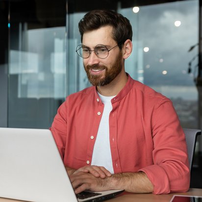Innovationsmanager sitzt an einem Schreibtisch und arbeitet konzentriert an einem Laptop in einem modernen Büroraum.