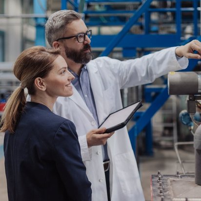 Zwei Personen stehen in einem Lager und prüfen eine Maschine.