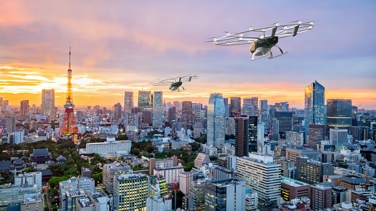 Futuristische Stadtansicht von Tokio bei Sonnenuntergang mit zwei Flugtaxis über der Skyline und dem Tokyo Tower im Hintergrund.