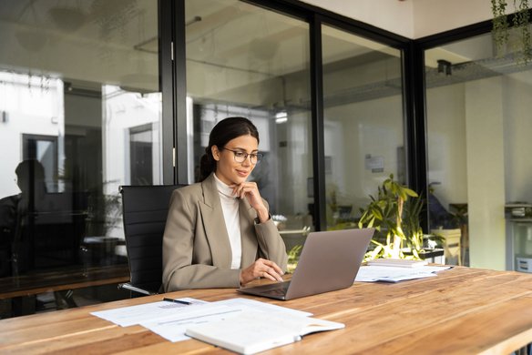 Frau im Business-Outfit arbeitet konzentriert an einem Laptop in einem modernen Büro.