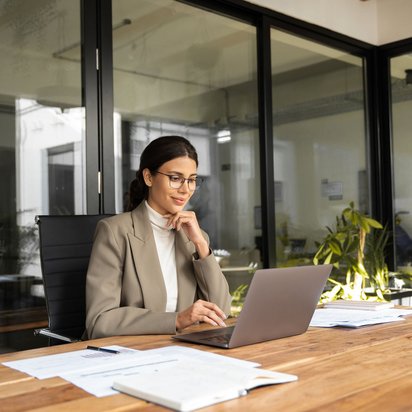 Frau im Business-Outfit arbeitet konzentriert an einem Laptop in einem modernen Büro.