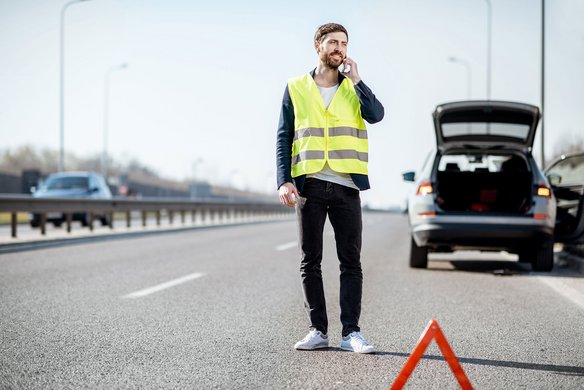 Person mit Warnweste auf einer Autobahn neben einem Pannenfahrzeug
