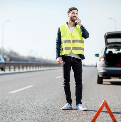 Person mit Warnweste auf einer Autobahn neben einem Pannenfahrzeug