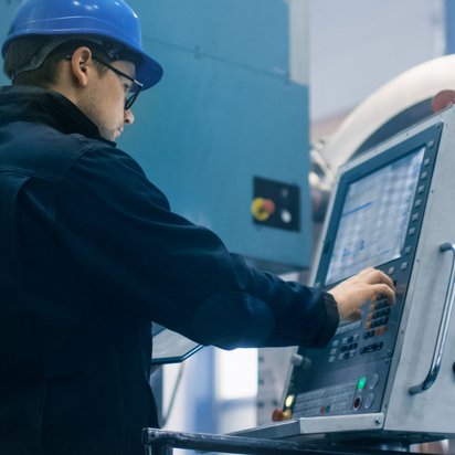 Techniker mit Schutzhelm bedient eine moderne CNC-Maschine in einer Produktionshalle