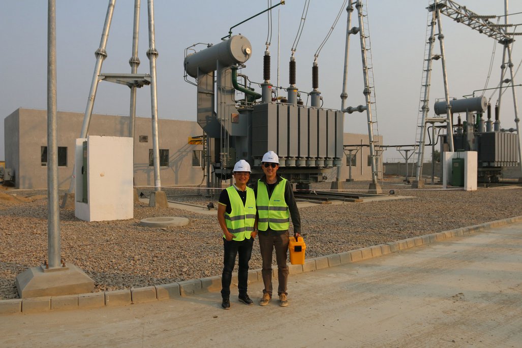 Die TÜV NORD China-Mitarbeiter Kevin Zhu und Alfie Jiang stehen vor dem Solarpark. Sie tragen Schutzhelme und Sicherheitswesten.