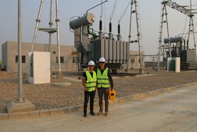 Die TÜV NORD China-Mitarbeiter Kevin Zhu und Alfie Jiang stehen vor dem Solarpark. Sie tragen Schutzhelme und Sicherheitswesten.