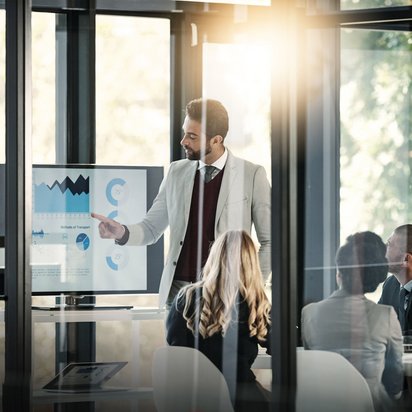 Strategiepräsentation mit Datenanalyse im modernen Meetingraum. Geschäftsmann präsentiert Diagramme auf einem Bildschirm vor Kollegen im Konferenzraum