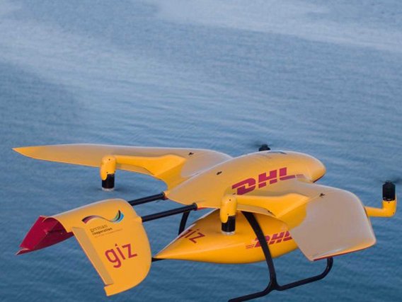 Eine gelbe DHL-Lieferdrohne mit vier Rotoren schwebt über Wasser und trägt das GIZ-Logo für Entwicklungszusammenarbeit.