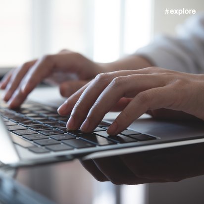 Nahaufnahme von Händen, die auf einer Laptop-Tastatur tippen. Im Hintergrund sind verschwommene Fenster zu sehen, die eine helle und moderne Arbeitsumgebung andeuten.