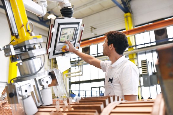 Mitarbeiter bedient ein Steuerungspanel an einer Industrieanlage in moderner Produktionshalle.